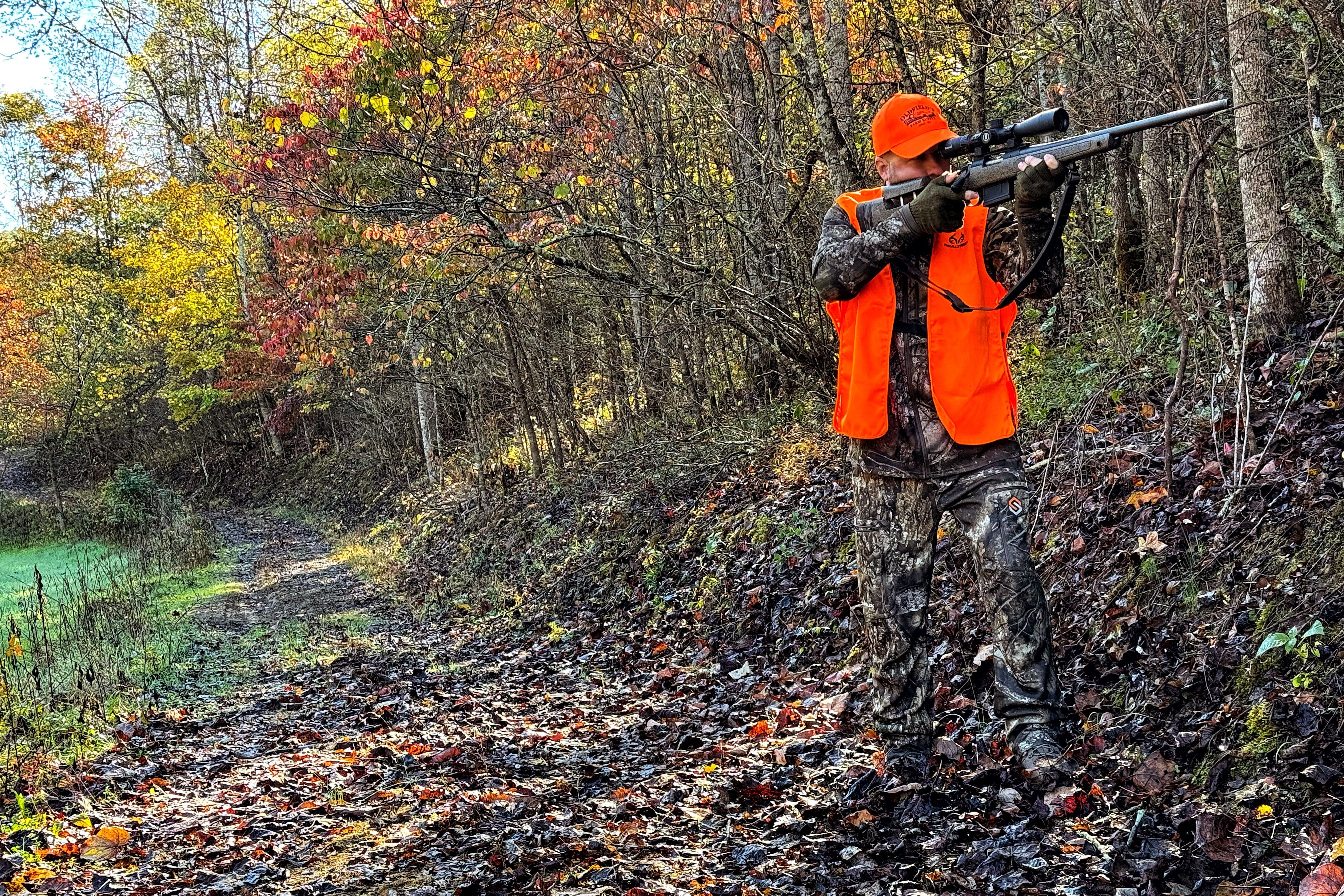 Deer hunter using a rifle in the woods wearing his blaze orange